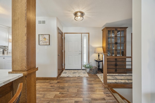 foyer with baseboards, a textured ceiling, visible vents, and dark wood-type flooring