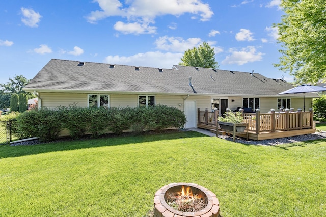 back of property featuring an outdoor fire pit, roof with shingles, a lawn, and a deck