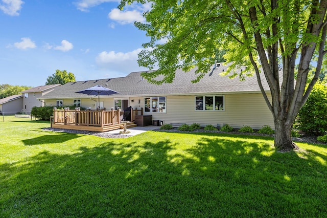 back of house featuring roof with shingles, a lawn, and a wooden deck