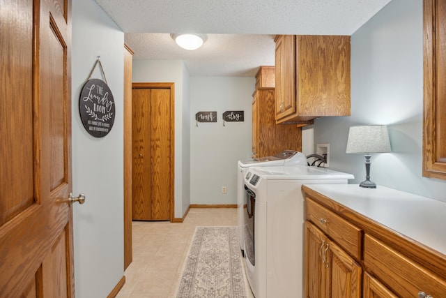 laundry room with a textured ceiling, light tile patterned floors, separate washer and dryer, baseboards, and cabinet space