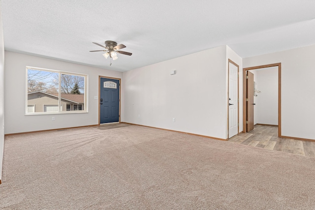 empty room with a textured ceiling, light colored carpet, baseboards, and ceiling fan