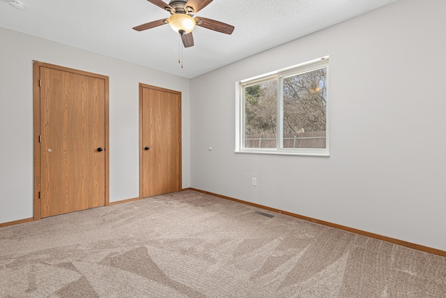 unfurnished bedroom featuring visible vents, carpet flooring, two closets, and baseboards