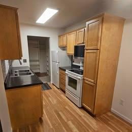 kitchen with white appliances, a sink, baseboards, light wood-type flooring, and dark countertops