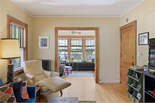 sitting room featuring ornamental molding, radiator, baseboards, and light wood finished floors