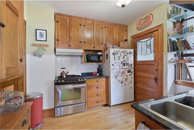 kitchen with dark countertops, freestanding refrigerator, under cabinet range hood, stainless steel range with gas cooktop, and black microwave