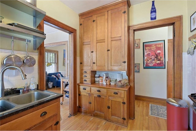 kitchen featuring dark countertops, decorative backsplash, light wood-style floors, brown cabinetry, and a sink