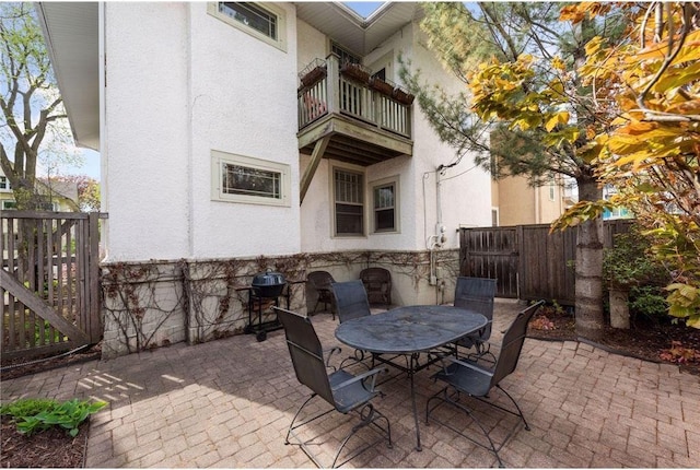 view of patio featuring outdoor dining space, fence, and a balcony