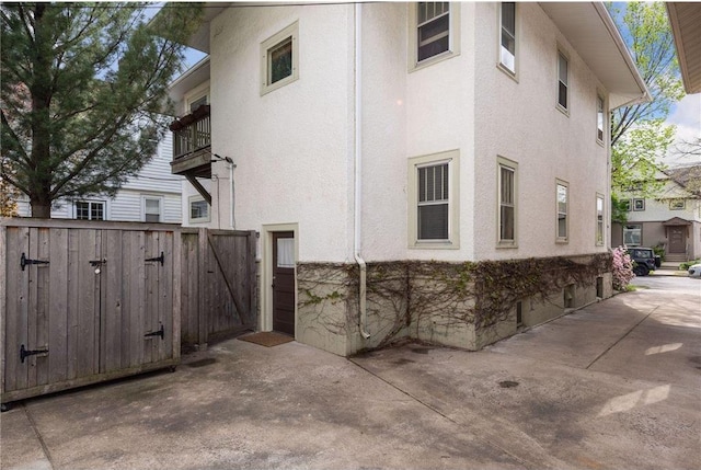 view of side of property featuring stone siding, a gate, fence, and stucco siding