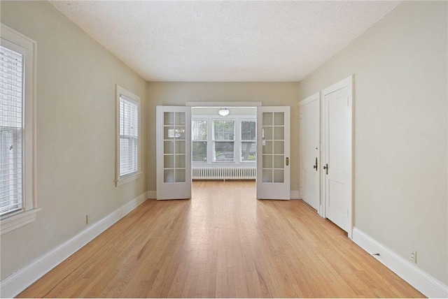 unfurnished room with light wood-type flooring, baseboards, a textured ceiling, and french doors