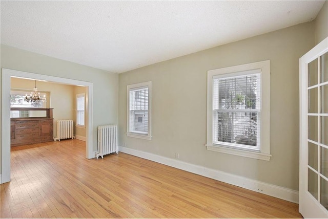 unfurnished room with baseboards, radiator heating unit, light wood-style flooring, and an inviting chandelier