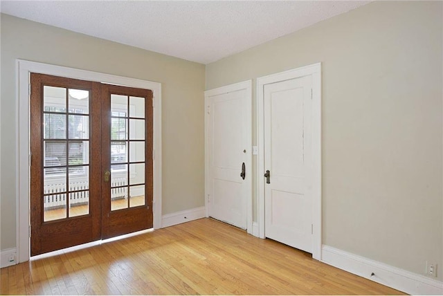 entryway featuring light wood-style floors, french doors, a textured ceiling, and baseboards