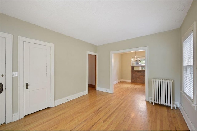 unfurnished room featuring radiator, light wood finished floors, baseboards, and an inviting chandelier