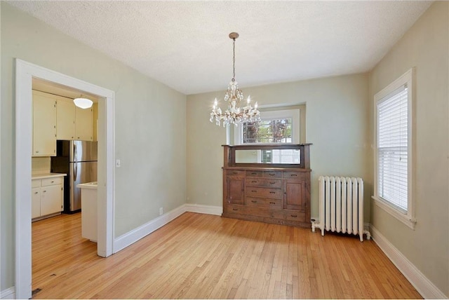 unfurnished dining area featuring a textured ceiling, baseboards, light wood-type flooring, radiator, and an inviting chandelier