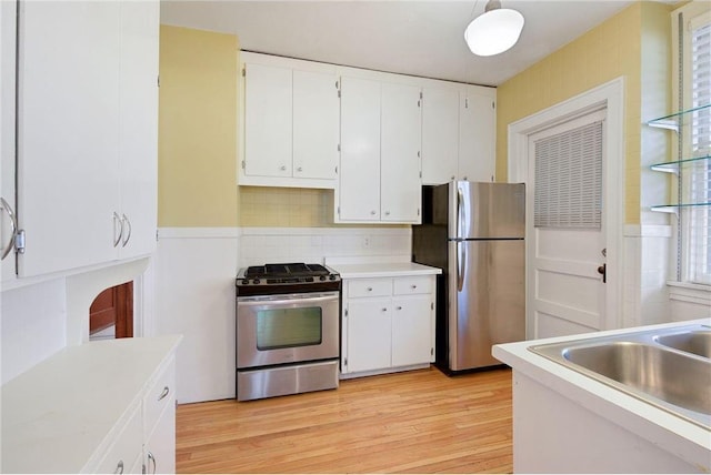 kitchen with a sink, white cabinetry, light wood-style floors, light countertops, and appliances with stainless steel finishes