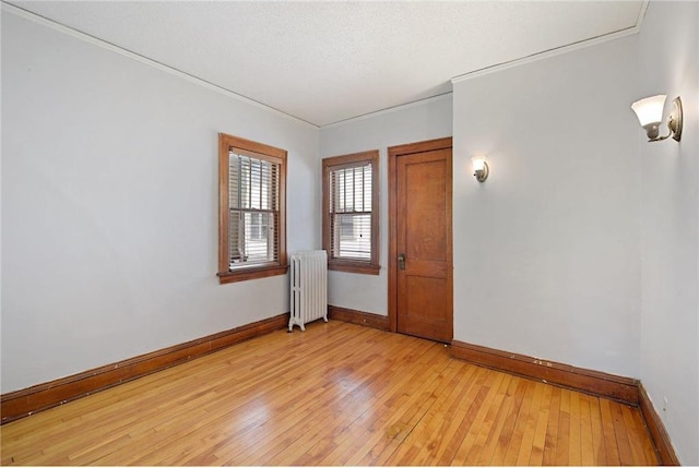 unfurnished room featuring a textured ceiling, light wood finished floors, radiator heating unit, and baseboards