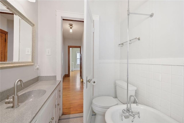 bathroom with toilet, a wainscoted wall, vanity, a freestanding tub, and tile walls