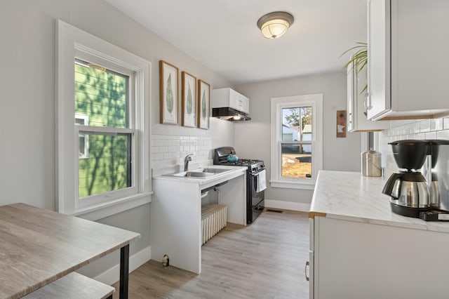 kitchen featuring under cabinet range hood, a sink, tasteful backsplash, gas stove, and light wood-style floors