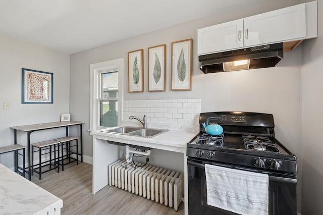 kitchen featuring black gas stove, under cabinet range hood, light wood-type flooring, white cabinets, and a sink