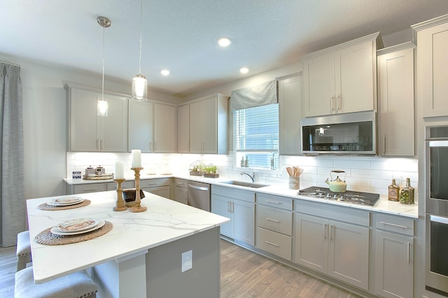 kitchen featuring light stone counters, gray cabinetry, a sink, hanging light fixtures, and appliances with stainless steel finishes