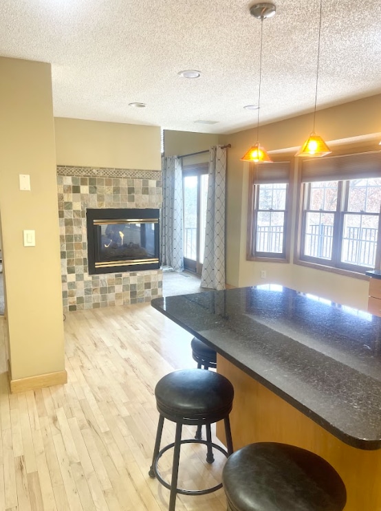 kitchen with a kitchen breakfast bar, open floor plan, light wood finished floors, a tiled fireplace, and pendant lighting