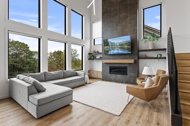 living area with baseboards, stairway, light wood-style flooring, a fireplace, and a high ceiling