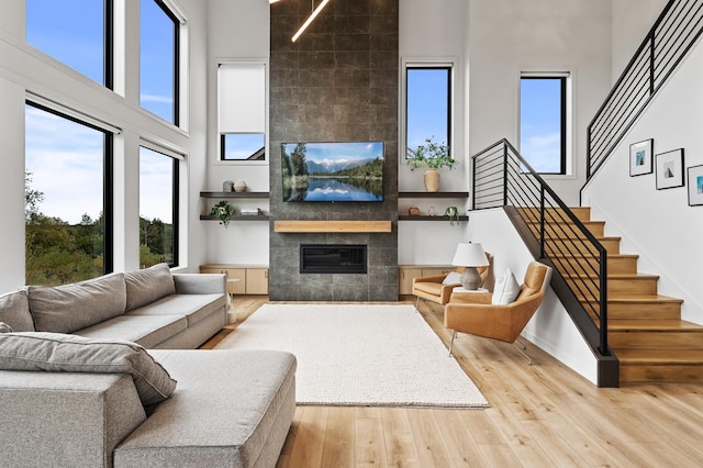 living area with a tiled fireplace, wood-type flooring, baseboards, a towering ceiling, and stairs