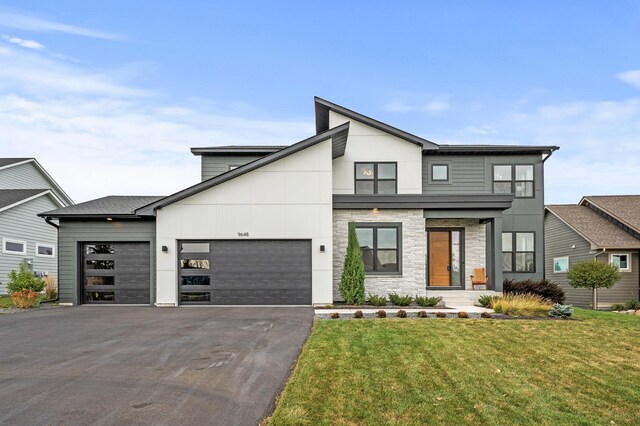 contemporary home featuring a front lawn, an attached garage, stone siding, and driveway