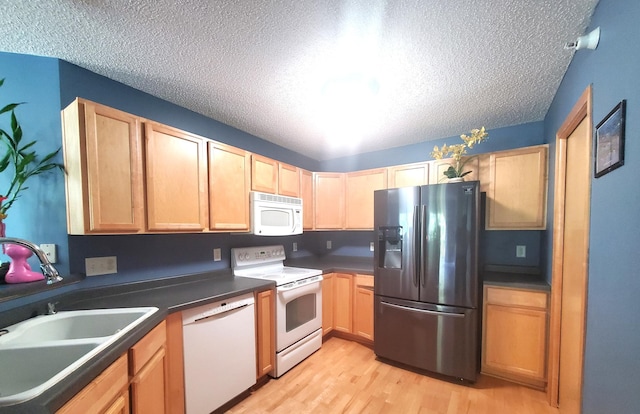 kitchen with white appliances, dark countertops, a textured ceiling, light wood-style floors, and a sink