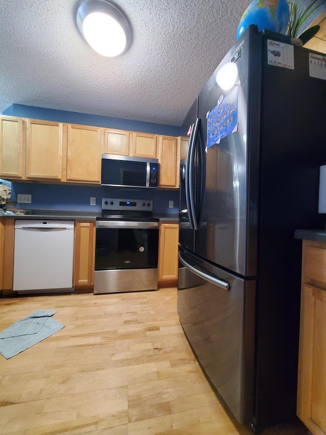 kitchen with light wood finished floors, appliances with stainless steel finishes, a textured ceiling, and dark countertops