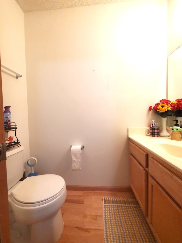 bathroom with wood finished floors, vanity, toilet, and baseboards