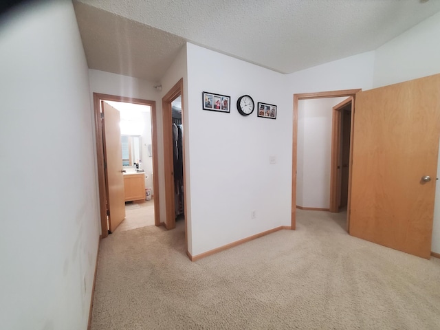 hall featuring light carpet, a textured ceiling, and baseboards