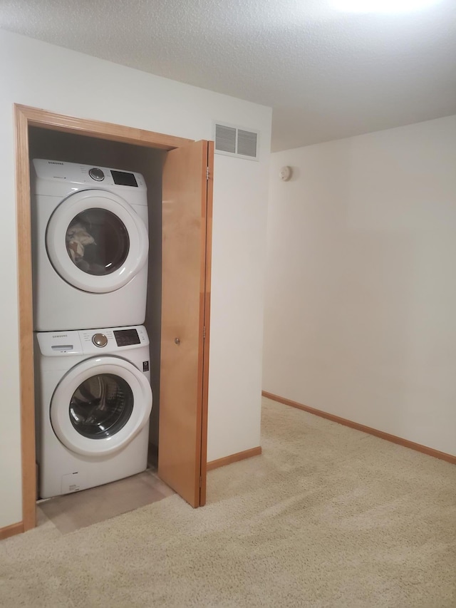 washroom featuring laundry area, baseboards, visible vents, stacked washer / dryer, and a textured ceiling