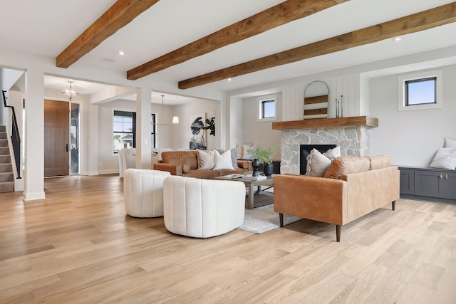 living area featuring a fireplace, stairway, light wood-style floors, a chandelier, and beamed ceiling