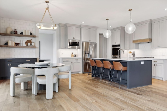 kitchen featuring a breakfast bar, a center island with sink, tasteful backsplash, light countertops, and appliances with stainless steel finishes