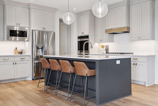 kitchen featuring a breakfast bar, light countertops, appliances with stainless steel finishes, light wood-type flooring, and under cabinet range hood