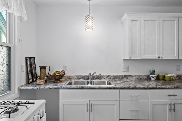 kitchen with dark countertops, white cabinets, a sink, and decorative light fixtures