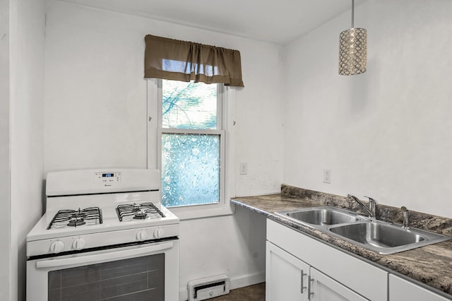 kitchen featuring white range with gas stovetop, dark countertops, decorative light fixtures, white cabinetry, and a sink