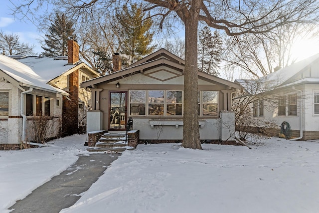 snow covered back of property with a chimney and stucco siding