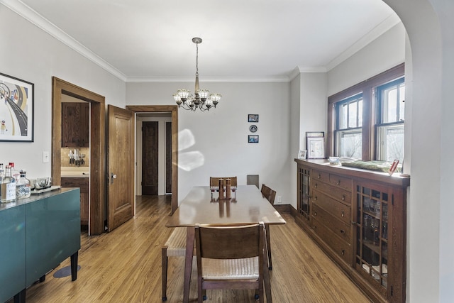 dining area with light wood-style floors, arched walkways, and crown molding