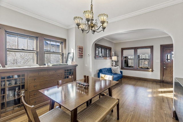 dining area featuring arched walkways, crown molding, and wood finished floors