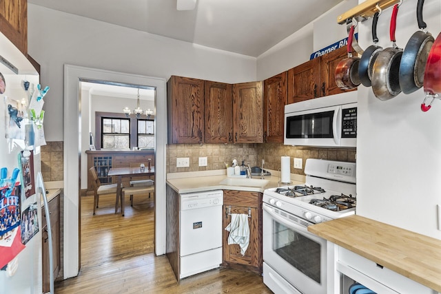 kitchen with a notable chandelier, light wood-style flooring, decorative backsplash, a sink, and white appliances