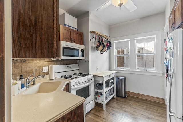 kitchen featuring white appliances, a sink, light countertops, dark wood-style floors, and tasteful backsplash