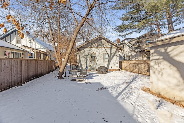 snow covered back of property featuring a fenced backyard and a chimney