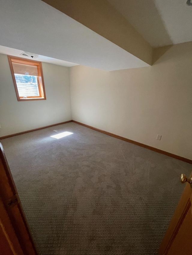 spare room featuring lofted ceiling, carpet flooring, and baseboards