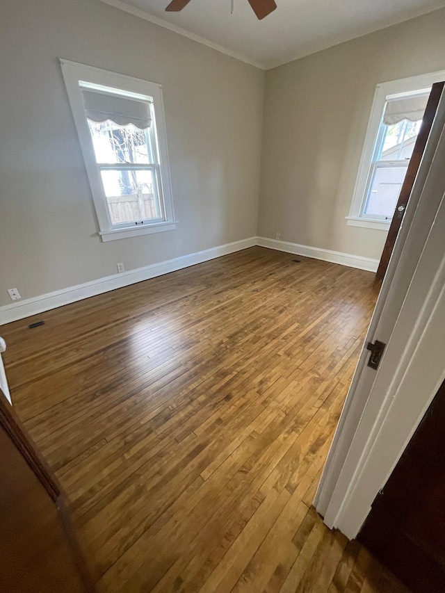 empty room featuring ceiling fan, wood finished floors, a wealth of natural light, and baseboards