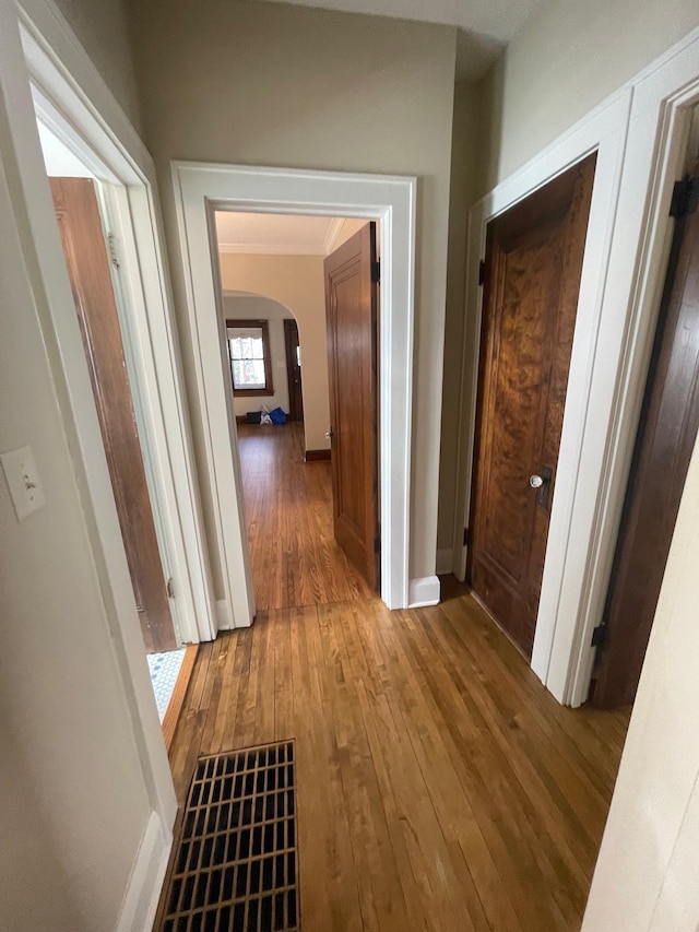 hallway with arched walkways, wood finished floors, and baseboards