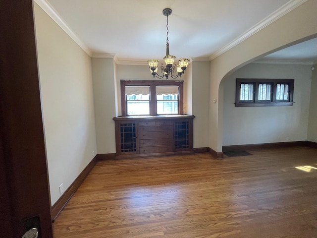 empty room with baseboards, arched walkways, wood finished floors, and ornamental molding