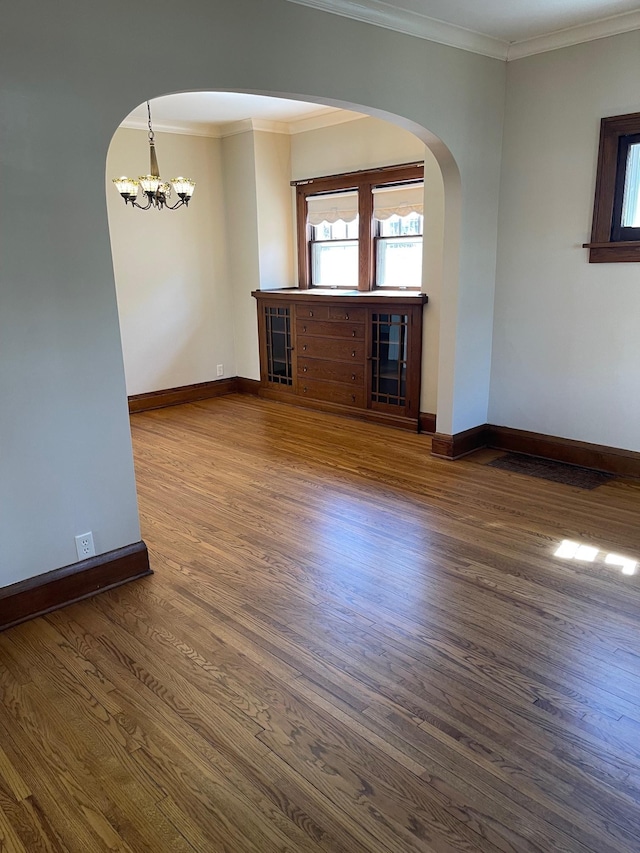 empty room with baseboards, arched walkways, ornamental molding, dark wood-type flooring, and an inviting chandelier