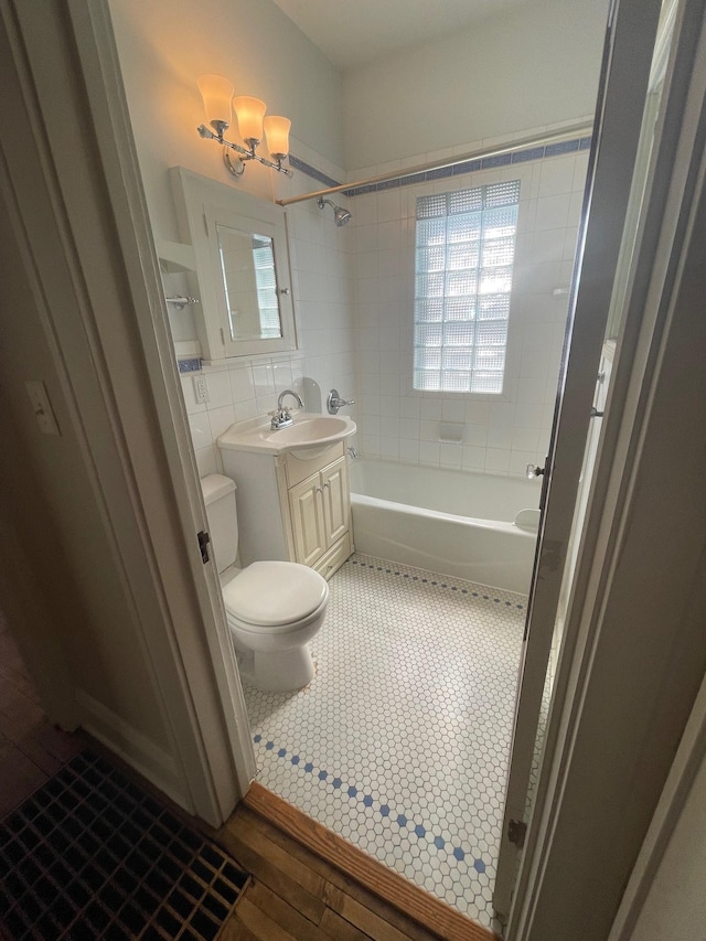 bathroom featuring toilet,  shower combination, tile patterned flooring, vanity, and tile walls