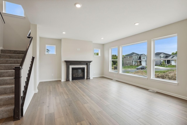 unfurnished living room with recessed lighting, baseboards, stairway, light wood finished floors, and a glass covered fireplace